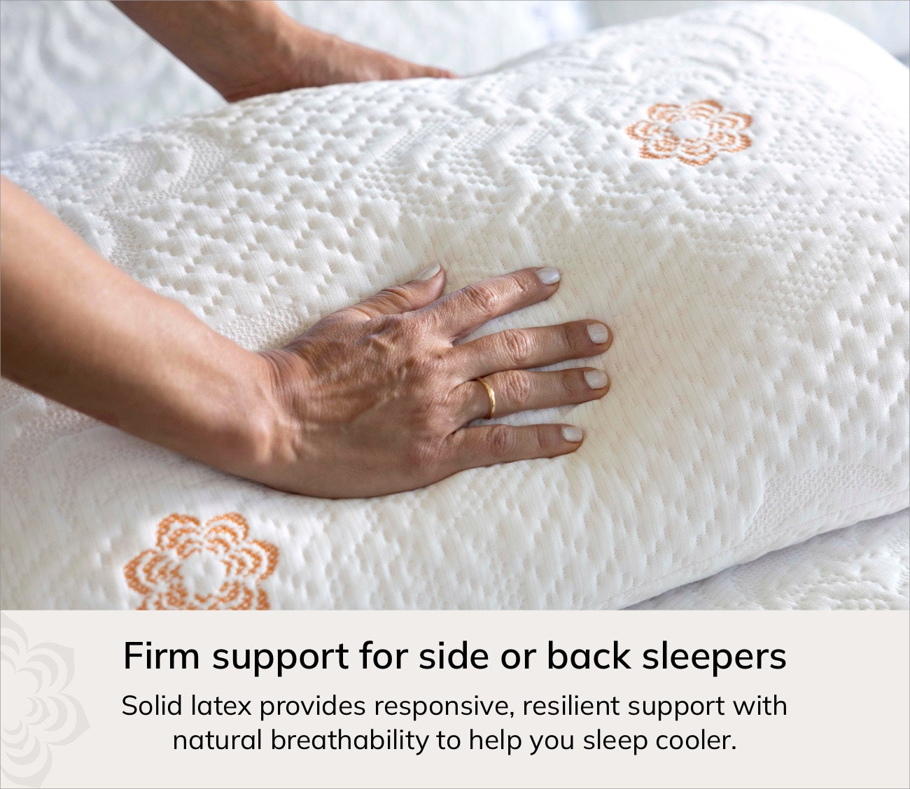 A close-up of Karma cooling pillow with orange embroidered floral details, being held by a person's hand to demonstrate its firm support. A text banner at the bottom reads: 'Firm support for side or back sleepers' and 'Solid latex provides responsive, resilient support with natural breathability to help you sleep cooler.
