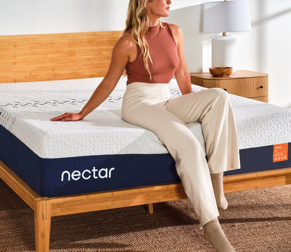 Woma sittin on Nectar 5.1 Ultra Memory Foam Mattress in a modern bedroom.
