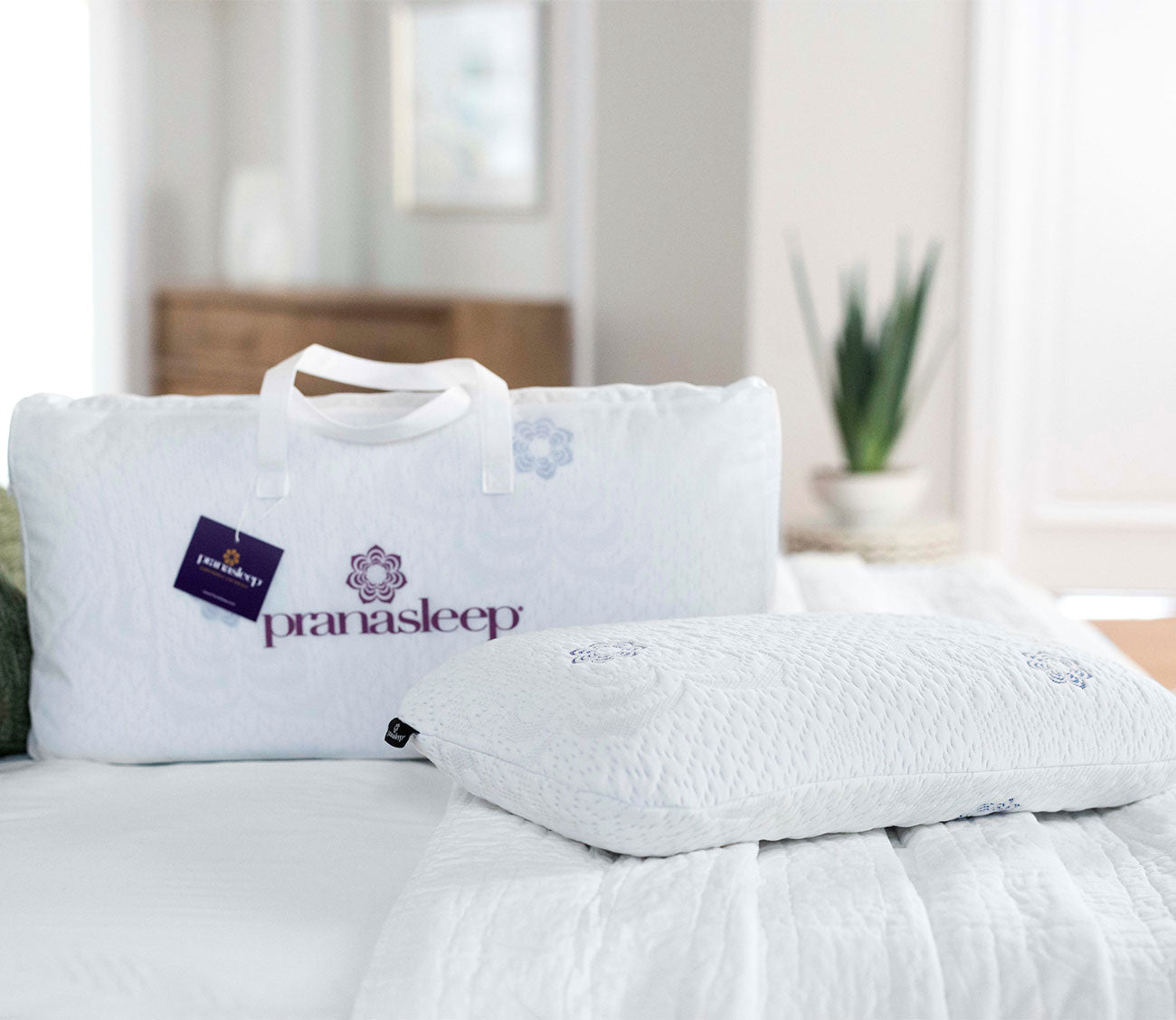 PranaSleep Asha Natural Latex Pillow displayed with branded carrying case in a serene bedroom setting.
