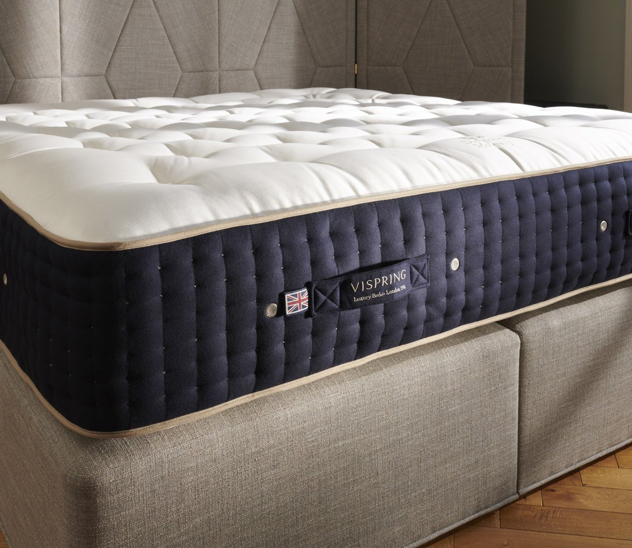 Angled view of a Vispring mattress featuring a plush hand-tufted top, navy side panels, and coordinating upholstered base.